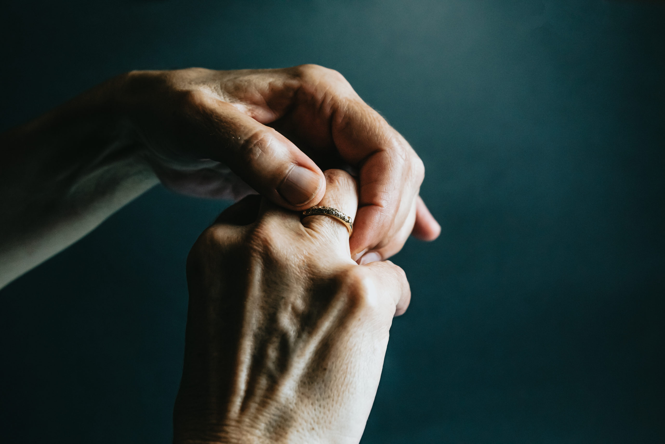 A pair of old hands grabbing a jewelry ring on the finger over a dark background